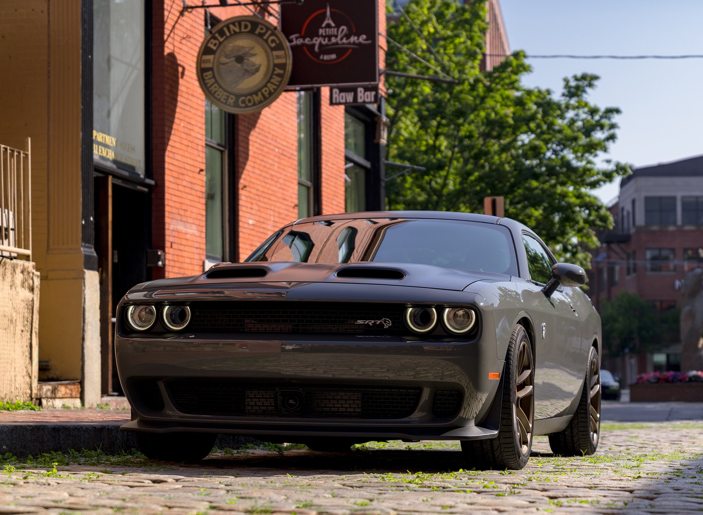 A dark gray 2019 Dodge Challenger SRT Hellcat, a big two-door high-performance car, parked on a cobblestone street.
