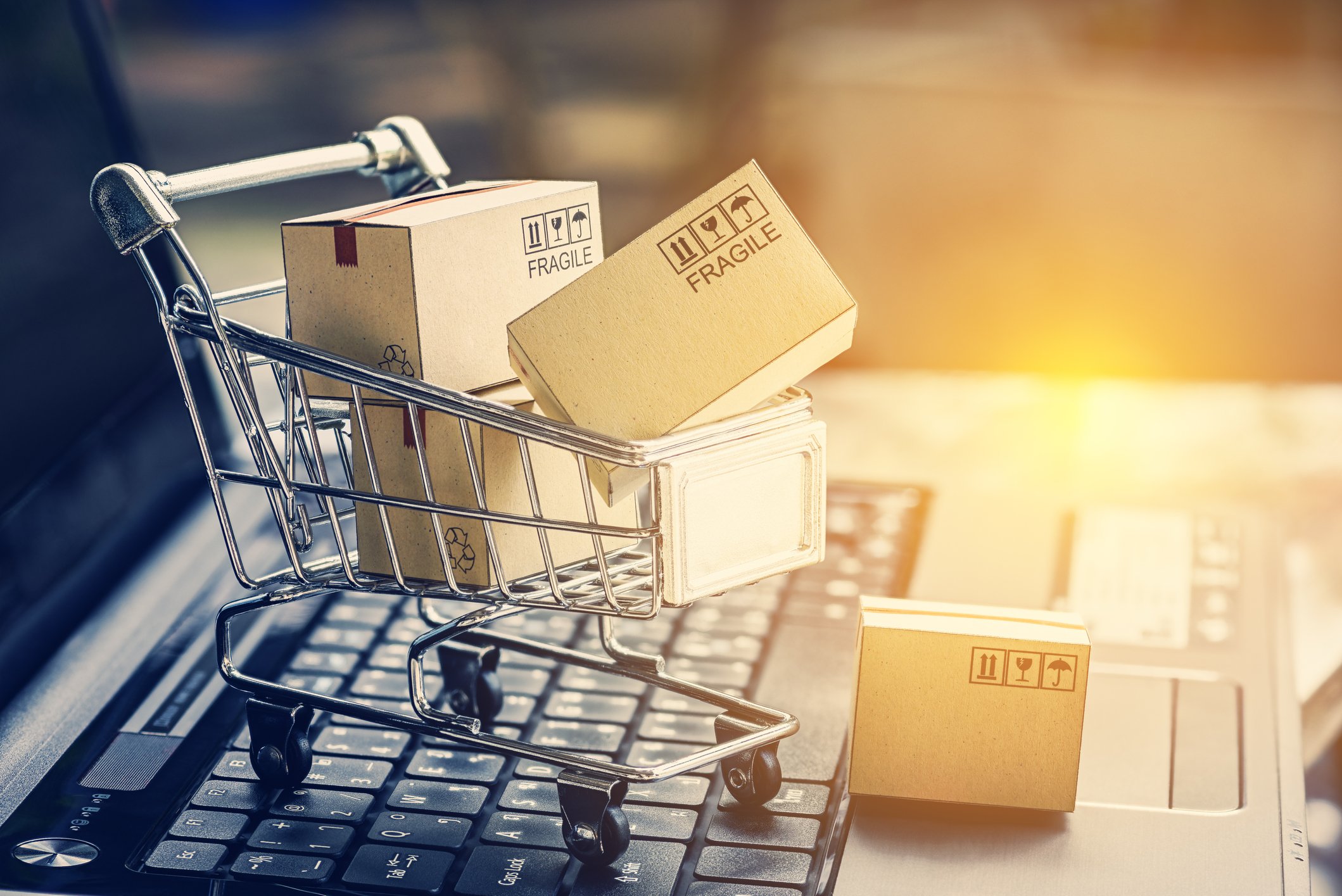Miniature boxes in a miniature shopping cart on top of a laptop keyboard.