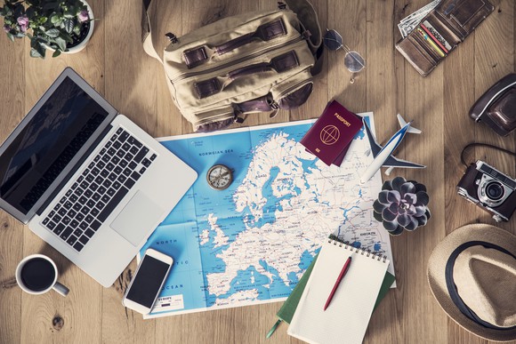 A laptop, passports, map, compass, and other travel-related items on a table