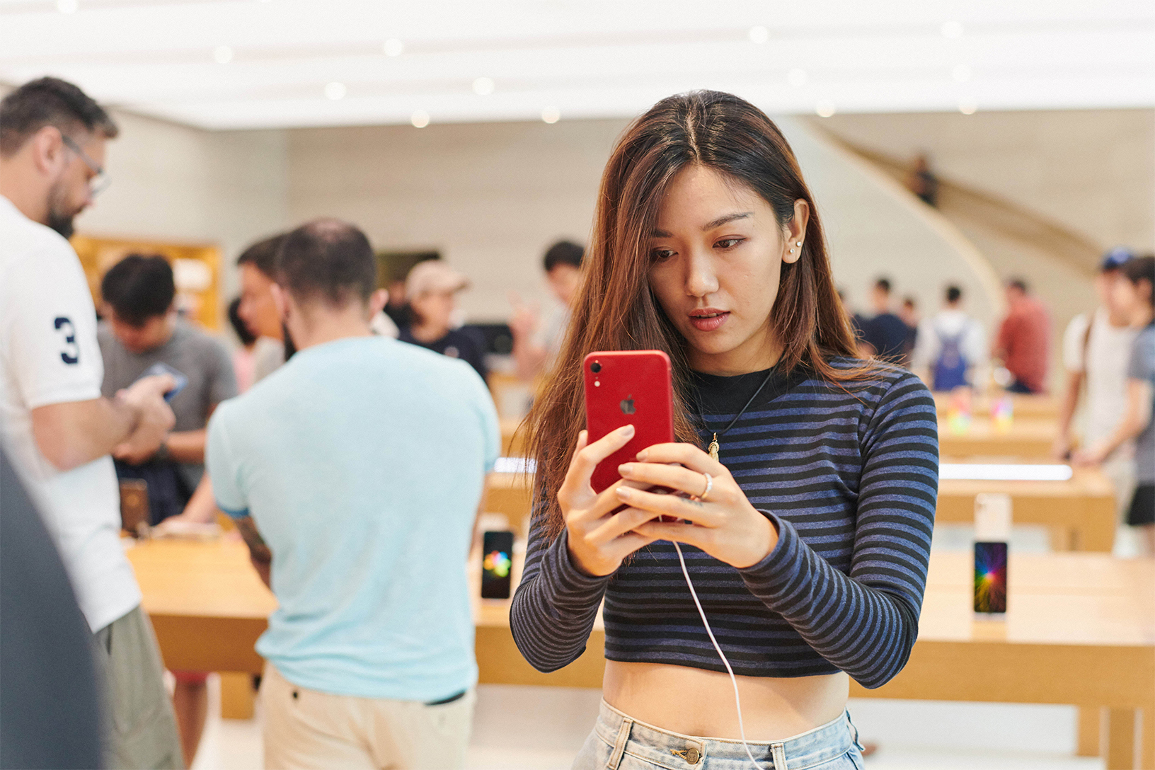 A woman looking at a red iPhone in an Apple store in Singapore.