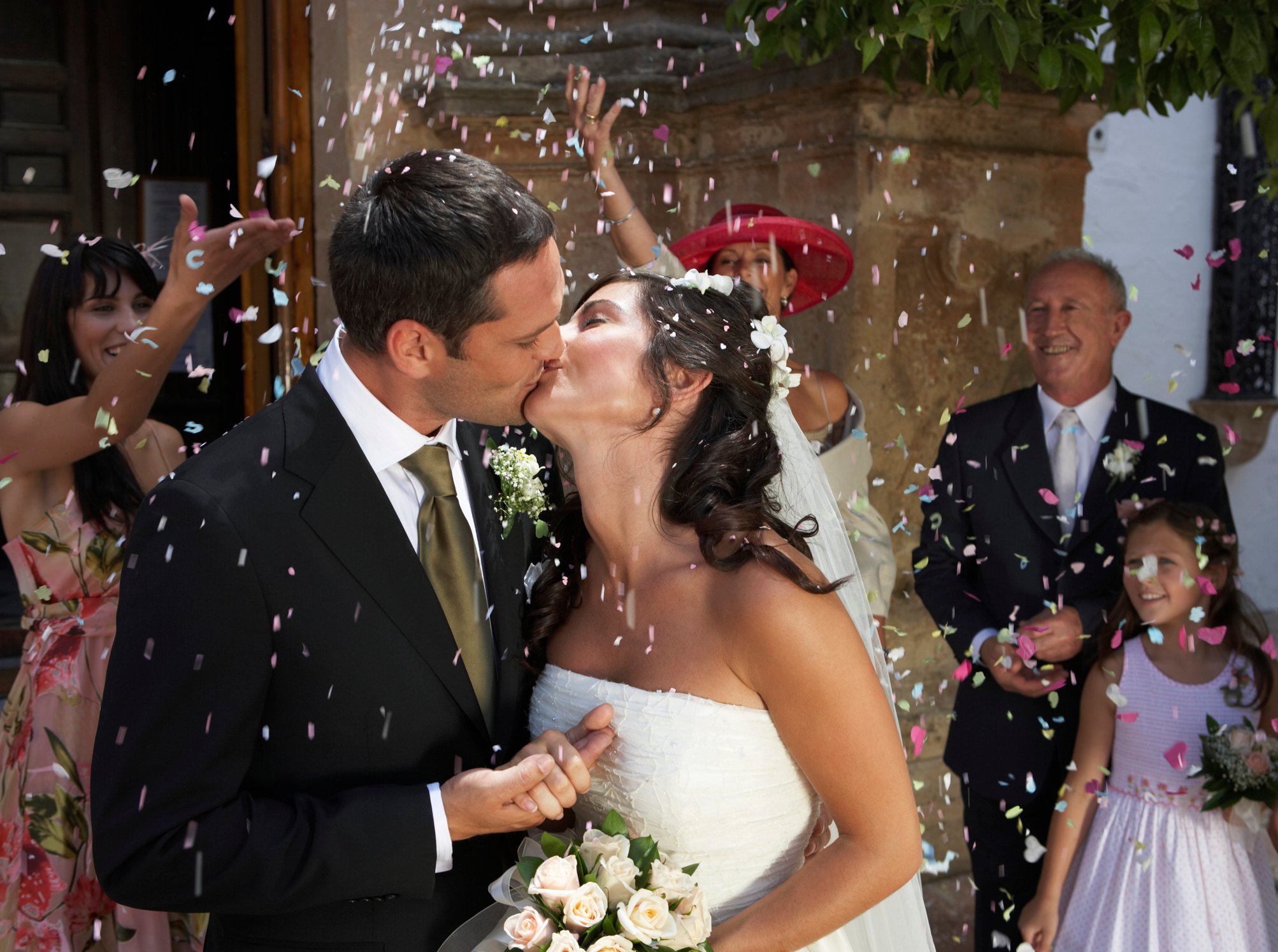 Bride and groom kissing while onlookers throw confetti