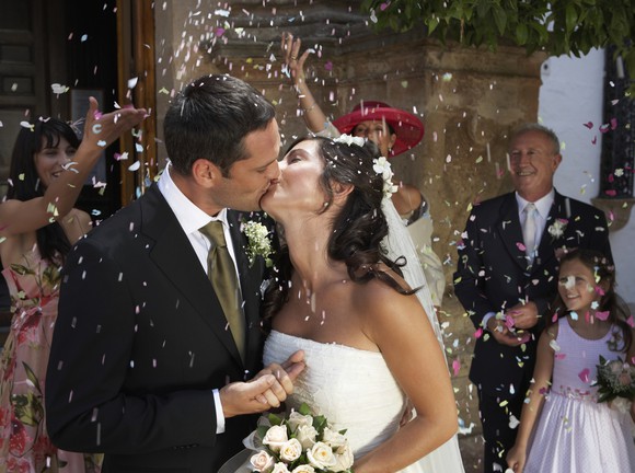 Bride and groom kissing while onlookers throw confetti