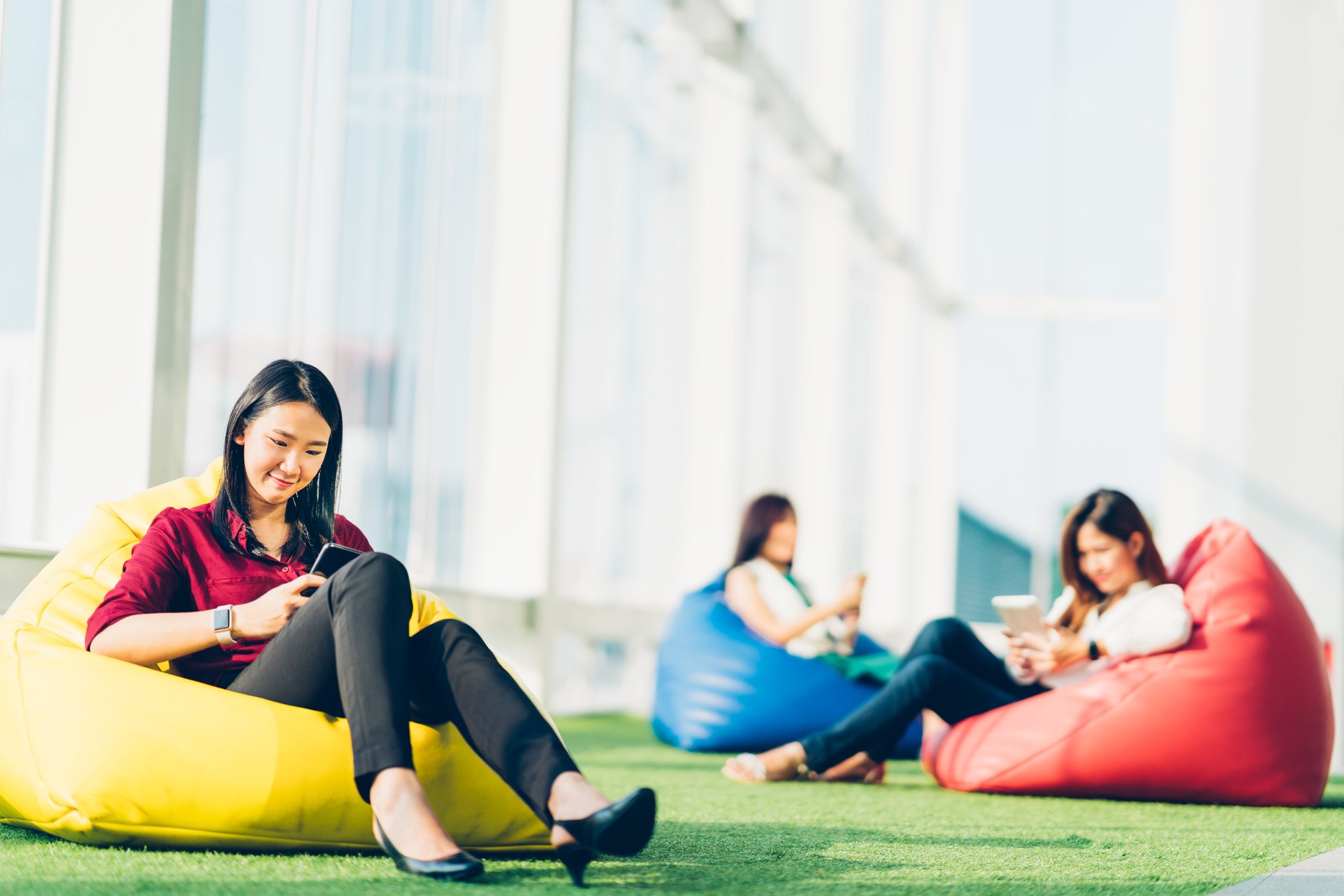 Three Asian women sitting on beanbag chairs while using mobile devices