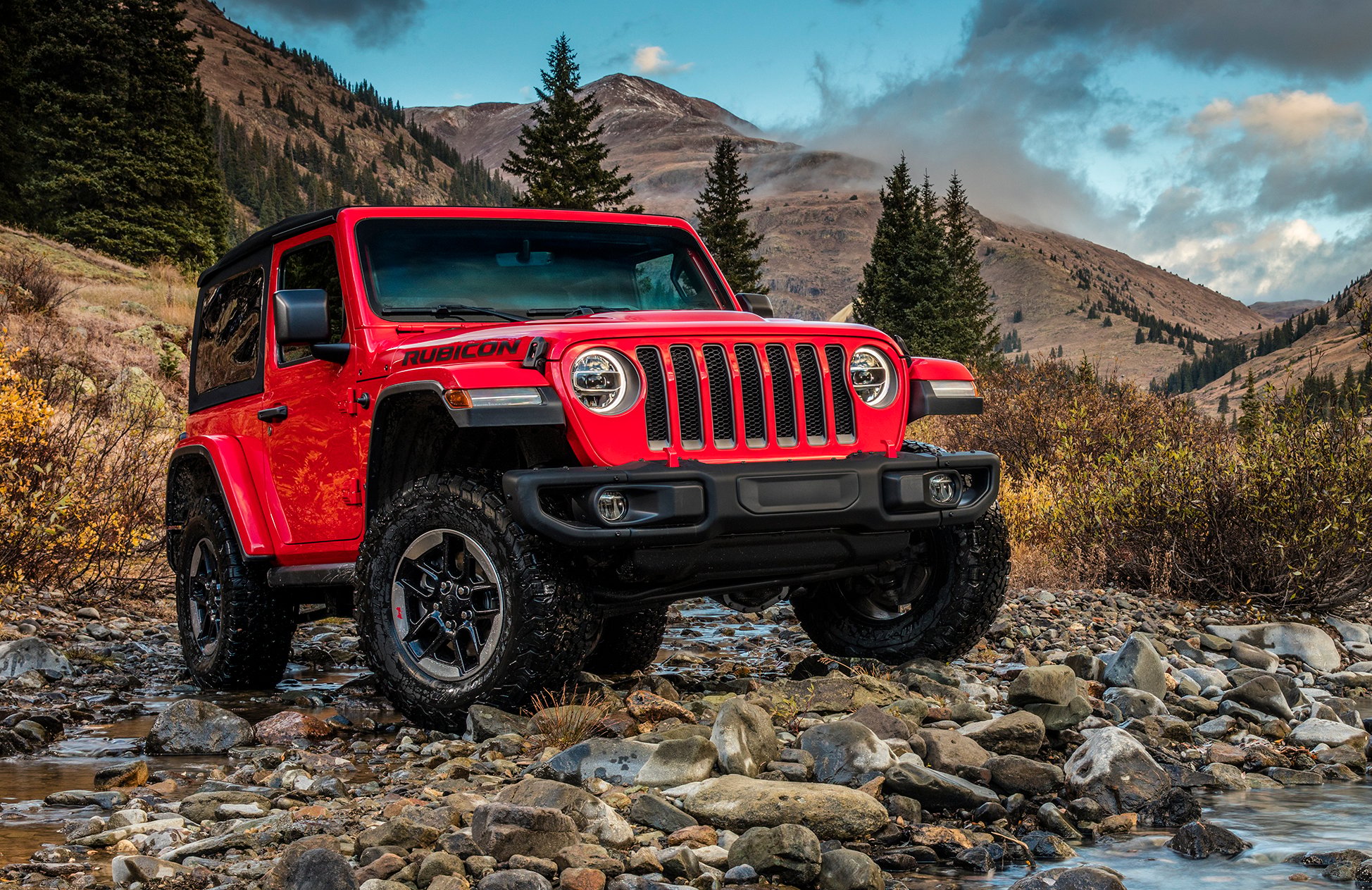 A red 2019 Jeep Wrangler Rubicon, an off-road SUV, shown on a rocky surface in the mountains.