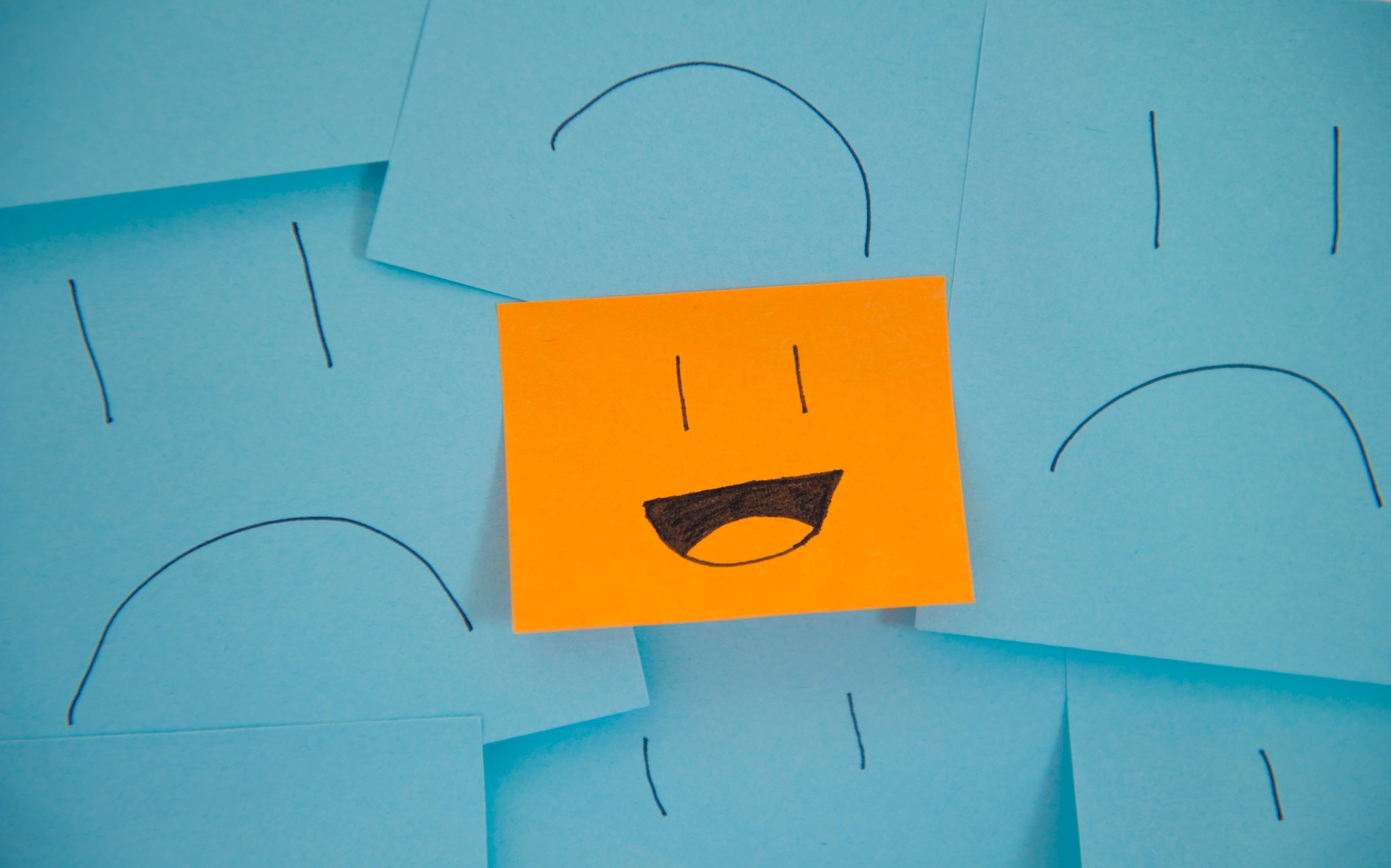 Blue sticky notes with sad faces with one orange sticky note with a smiley face
