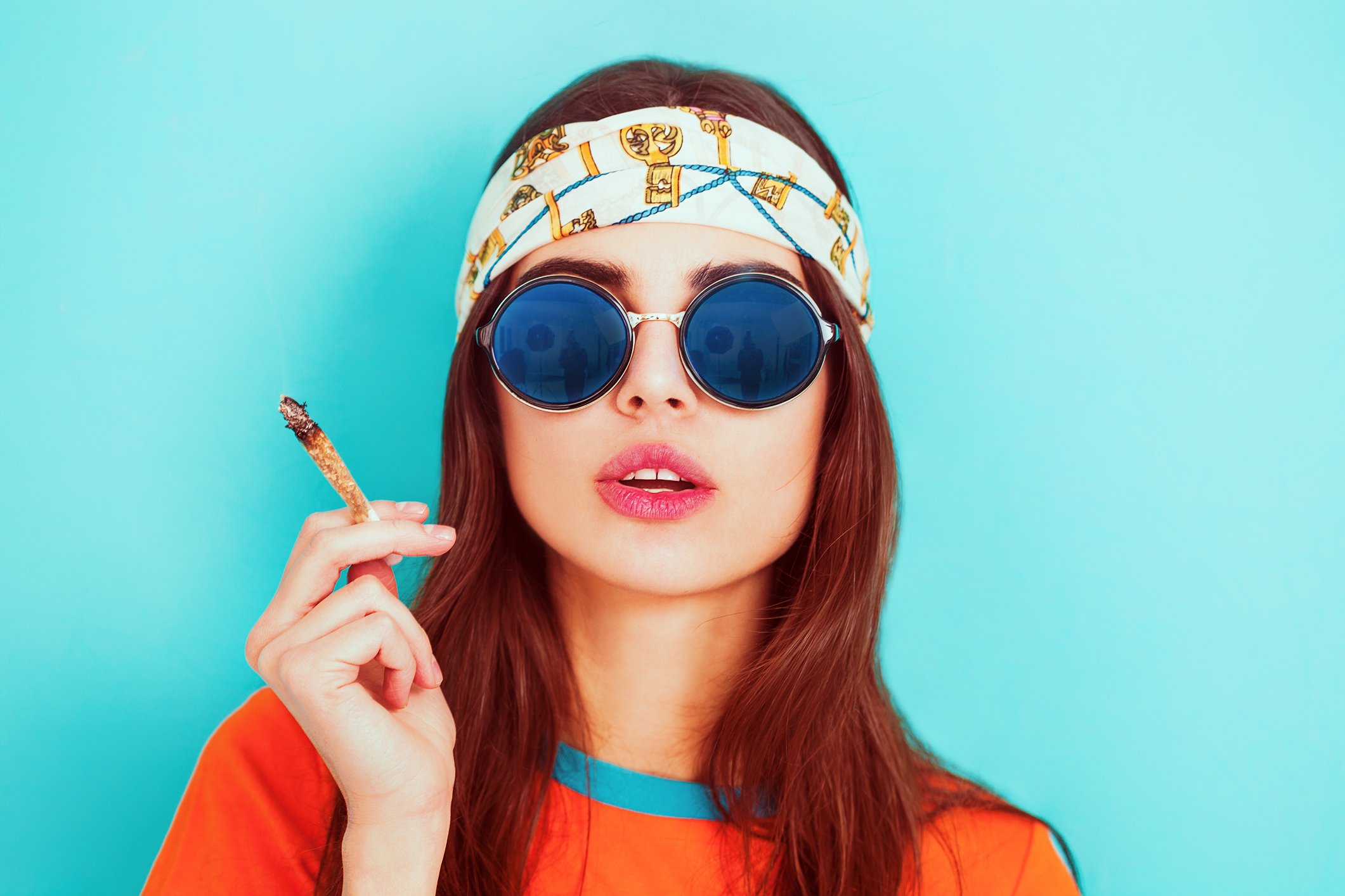 A young woman wearing a bandanna and sunglasses and smoking a joint.