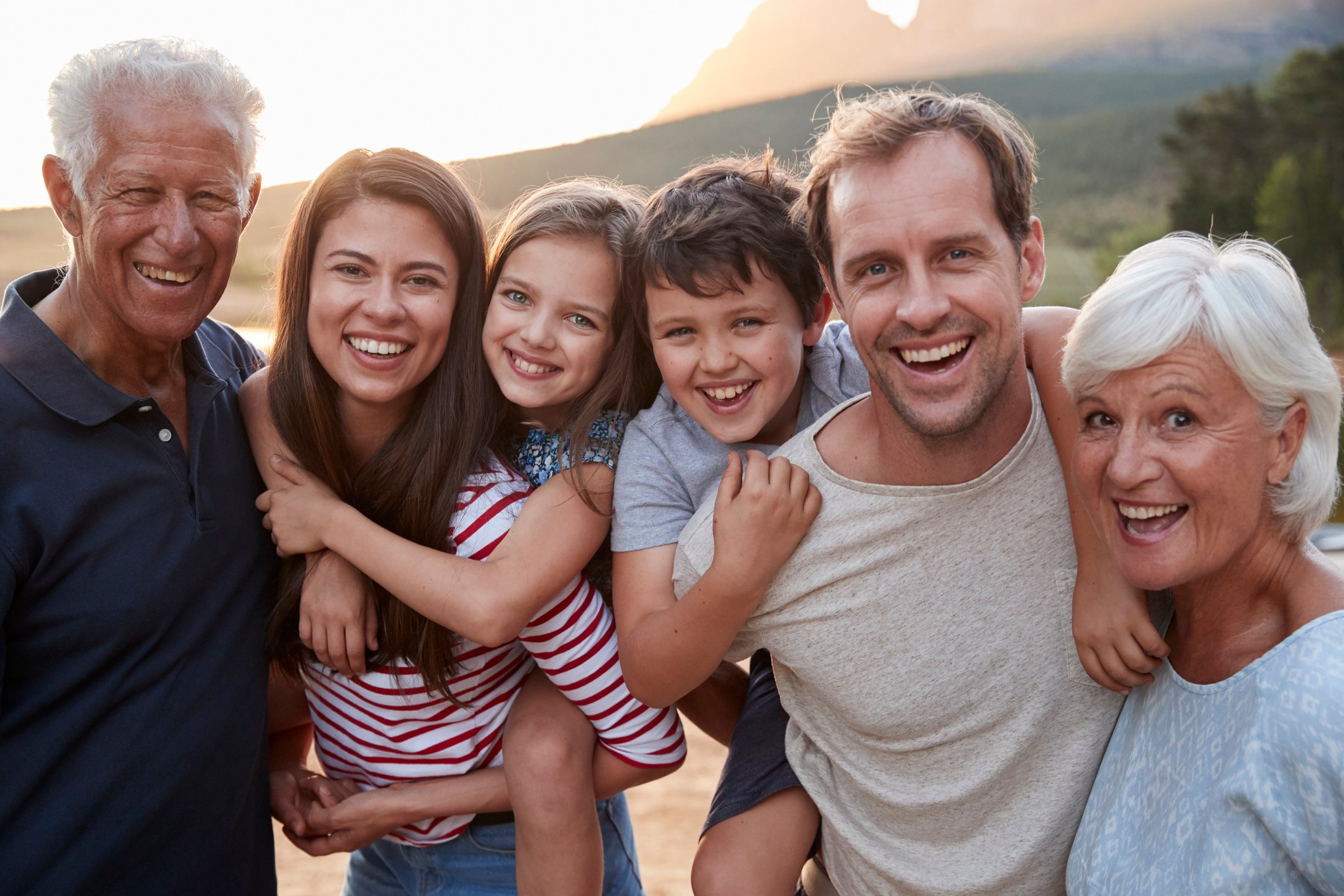 Older man, young woman, young girl, young boy, young man, and older woman in a row outdoors.