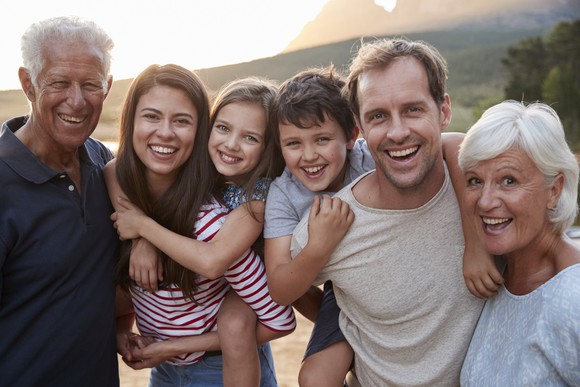 Older man, young woman, young girl, young boy, young man, and older woman in a row outdoors.