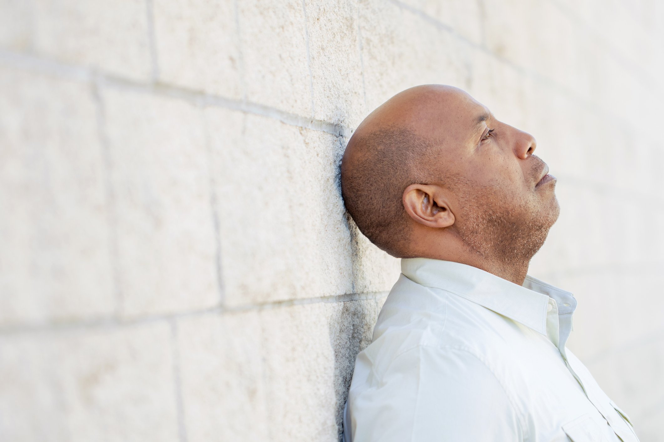 Man with sad expression leaning against a wall