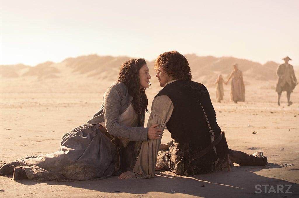A man and woman sitting on the ground in the desert facing each other.
