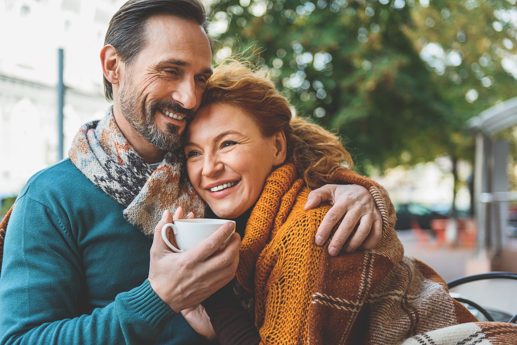 An older couple smile as they embrace outdoors.