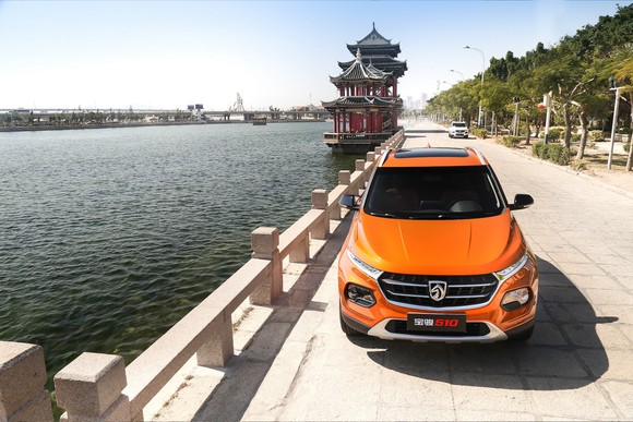 An orange Baojun 510, a compact crossover SUV, parked on a waterfront road in China.
