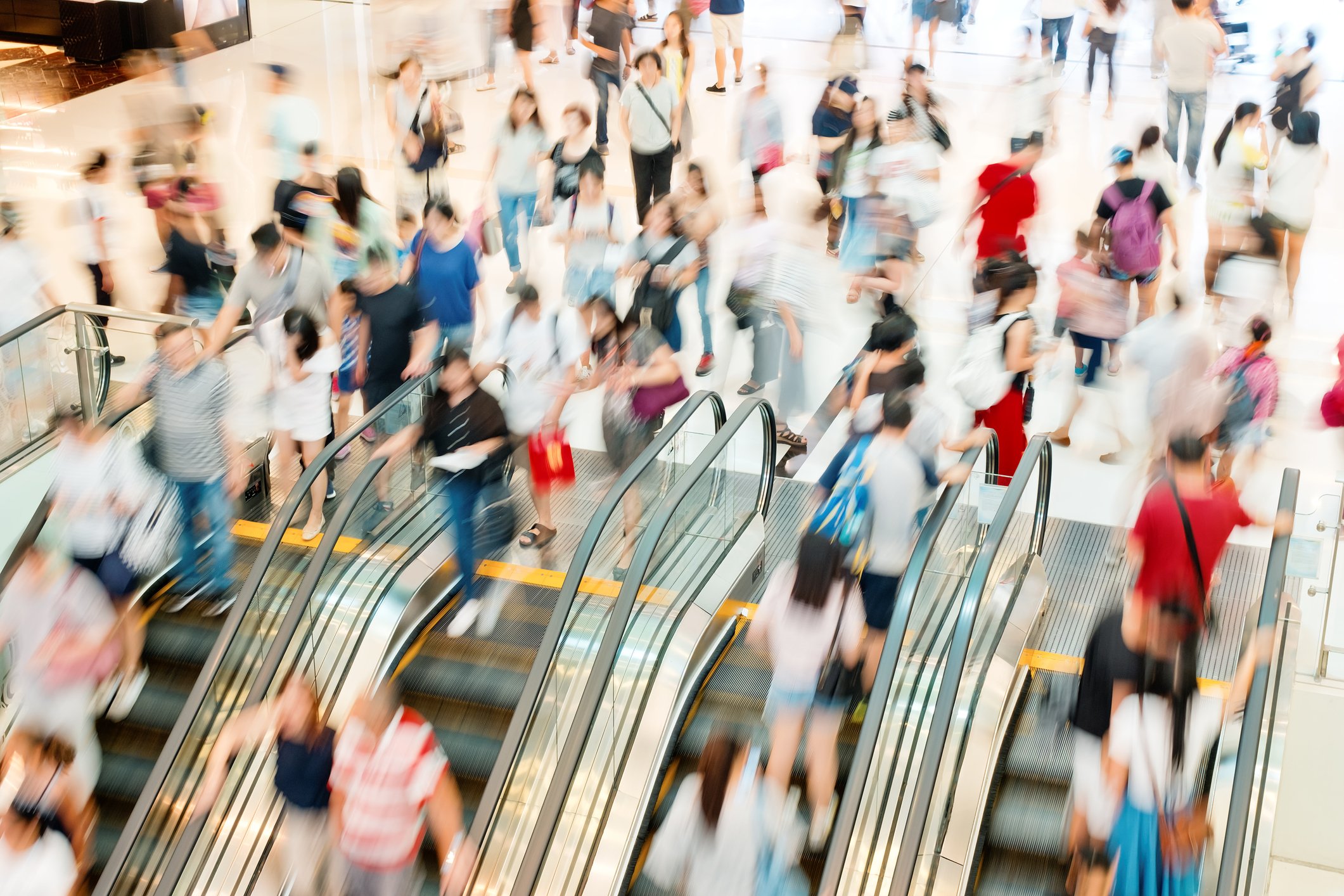A blurred group of shoppers moving up and down escalators at a shopping mall