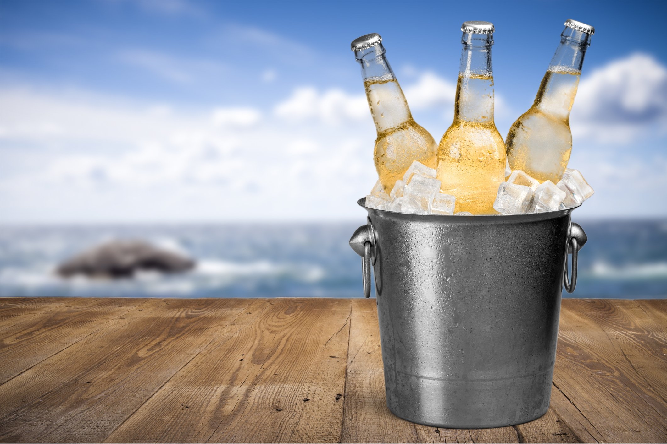 A bucket of beers on a deck with the ocean in the background.