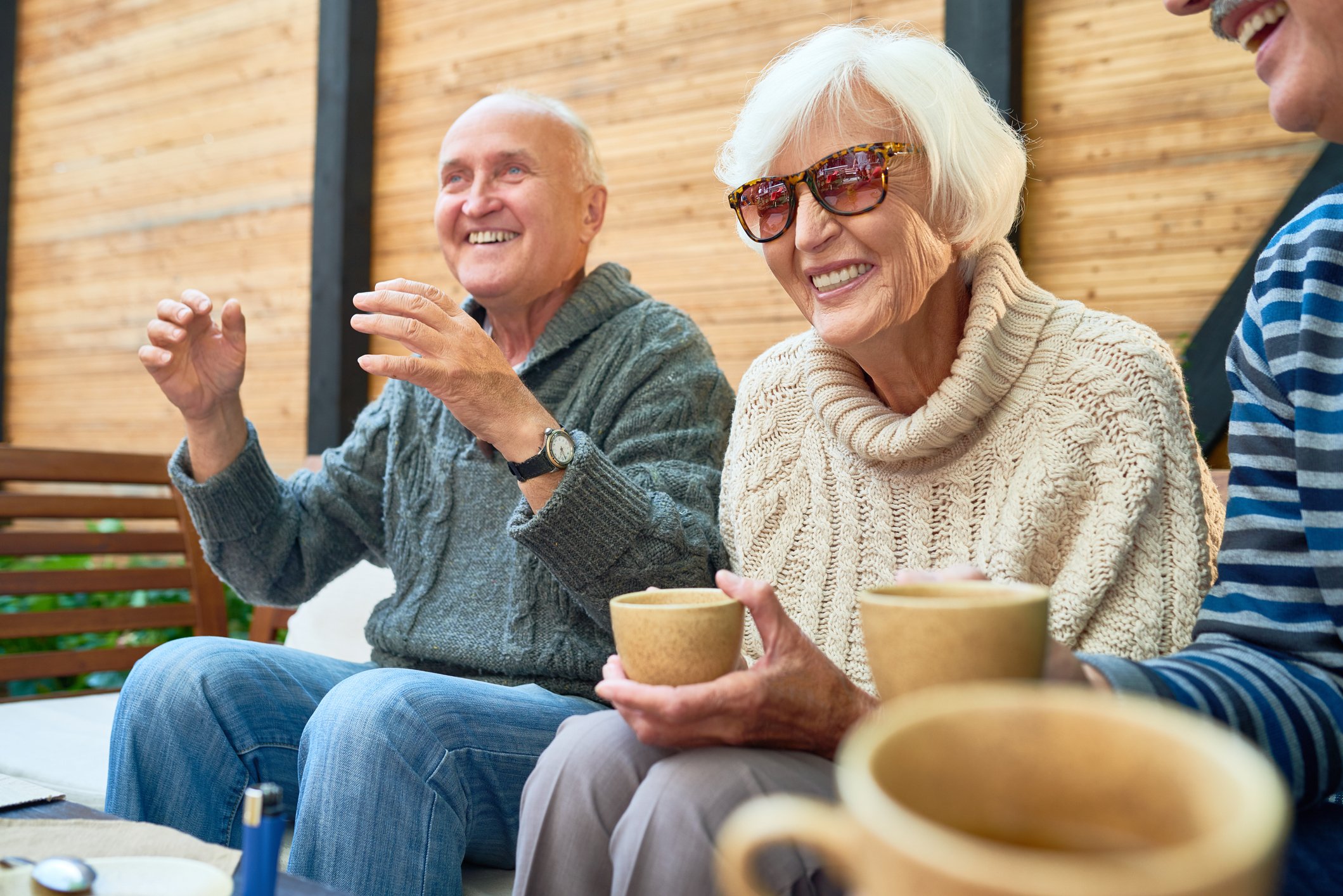 Smiling older woman in sunglasses sitting between two men.