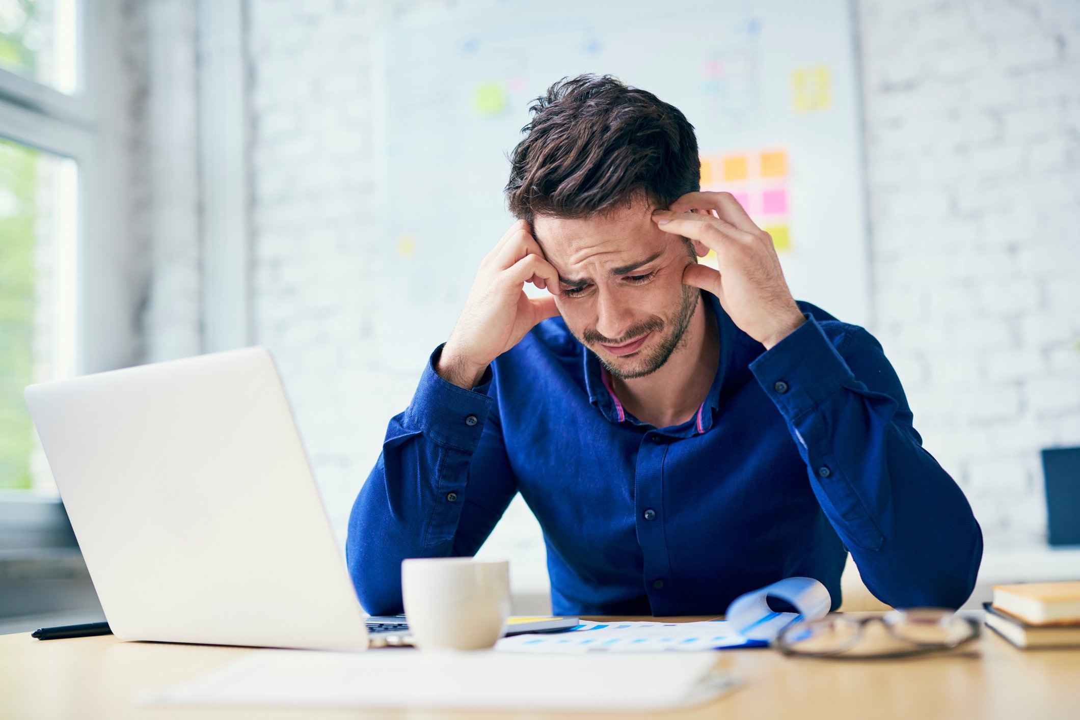 Man at laptop holding his head and scrunching his face