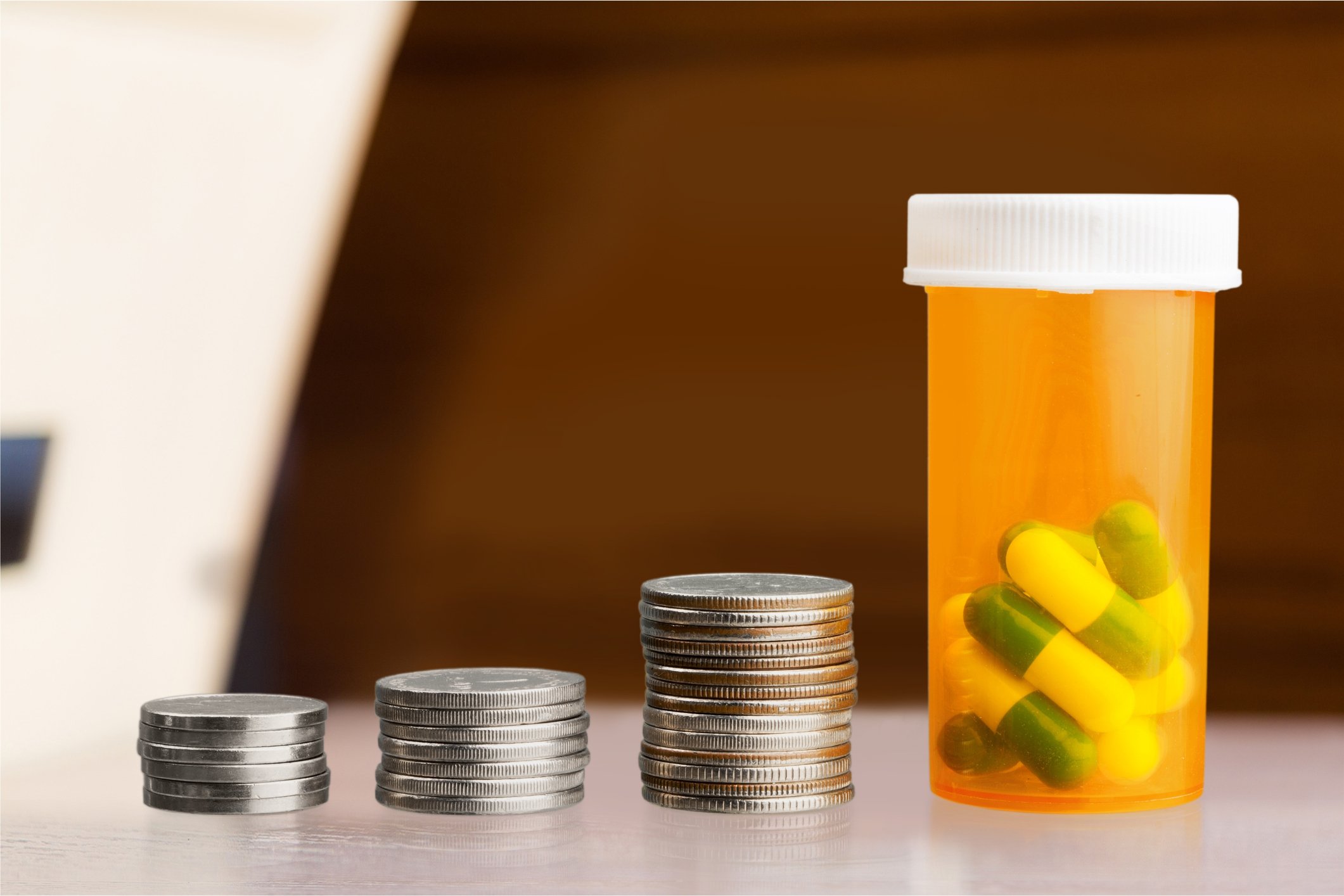 Increasingly higher stacks of coins with a pill bottle at the end of the row