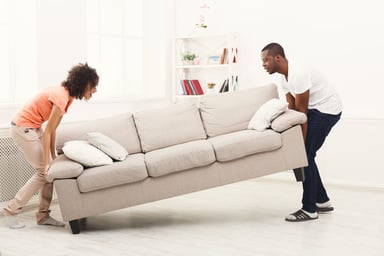 A man and woman moving a sofa in their home.