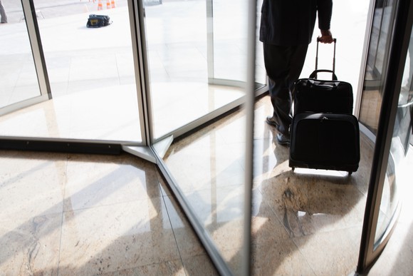 Man walking out of a revolving door, pulling a wheeled bag