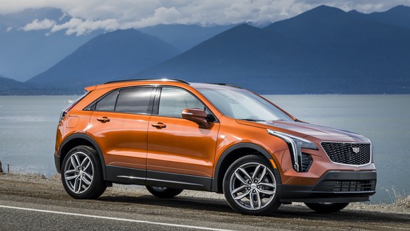 An orange 2019 Cadillac XT4, a compact luxury crossover, parked next to a lake. 
