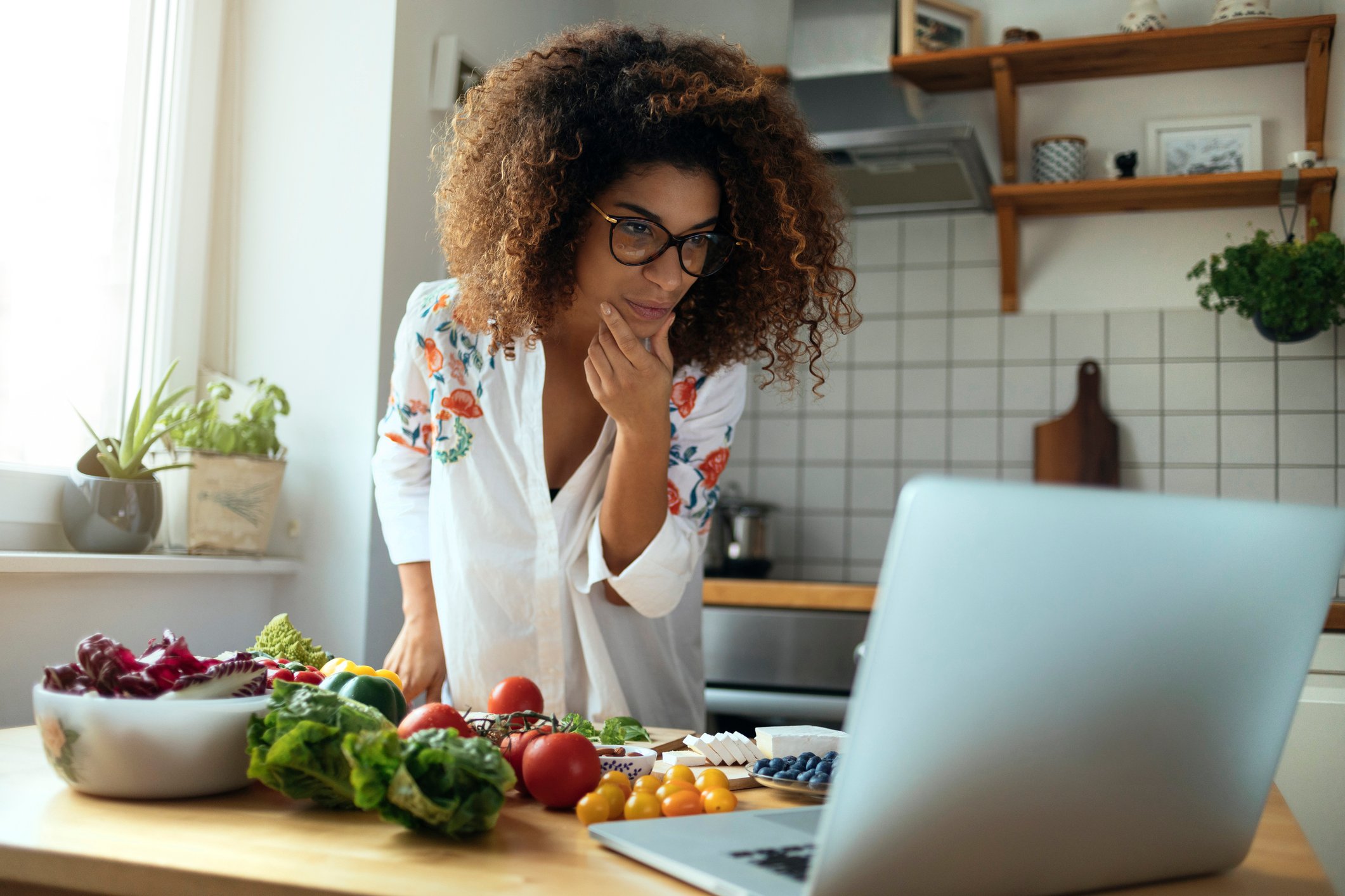 A woman looks at a computer while she cooks.