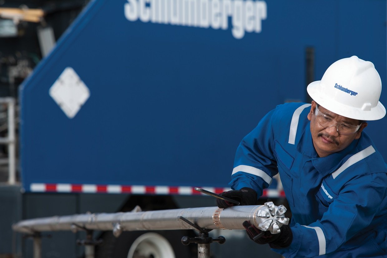 Person wearing Schlumberger hard hat holding a drill bit in front of a trailer.
