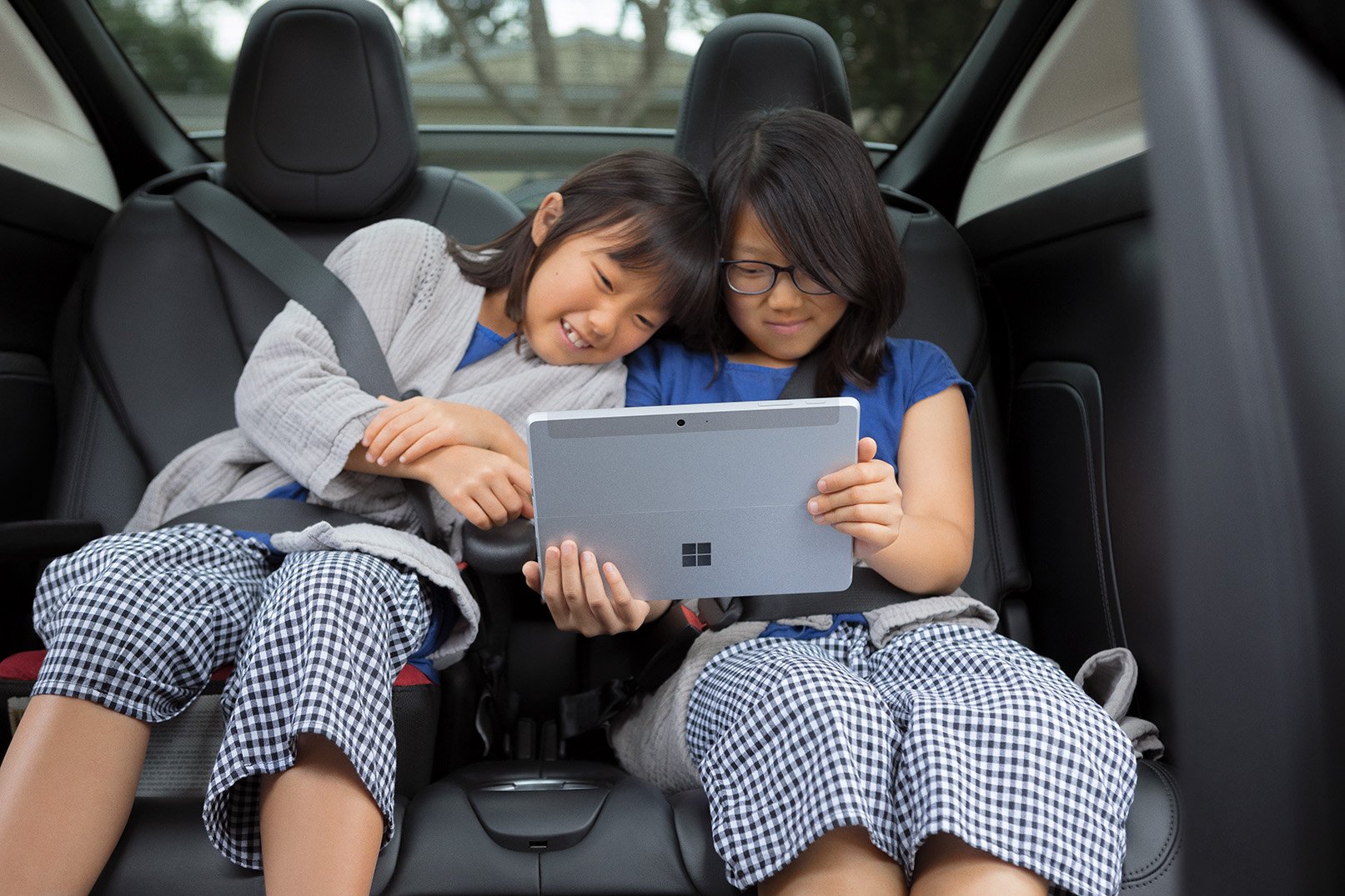 Two children watching a movie on a Microsoft Surface tablet in the back seat of a car.