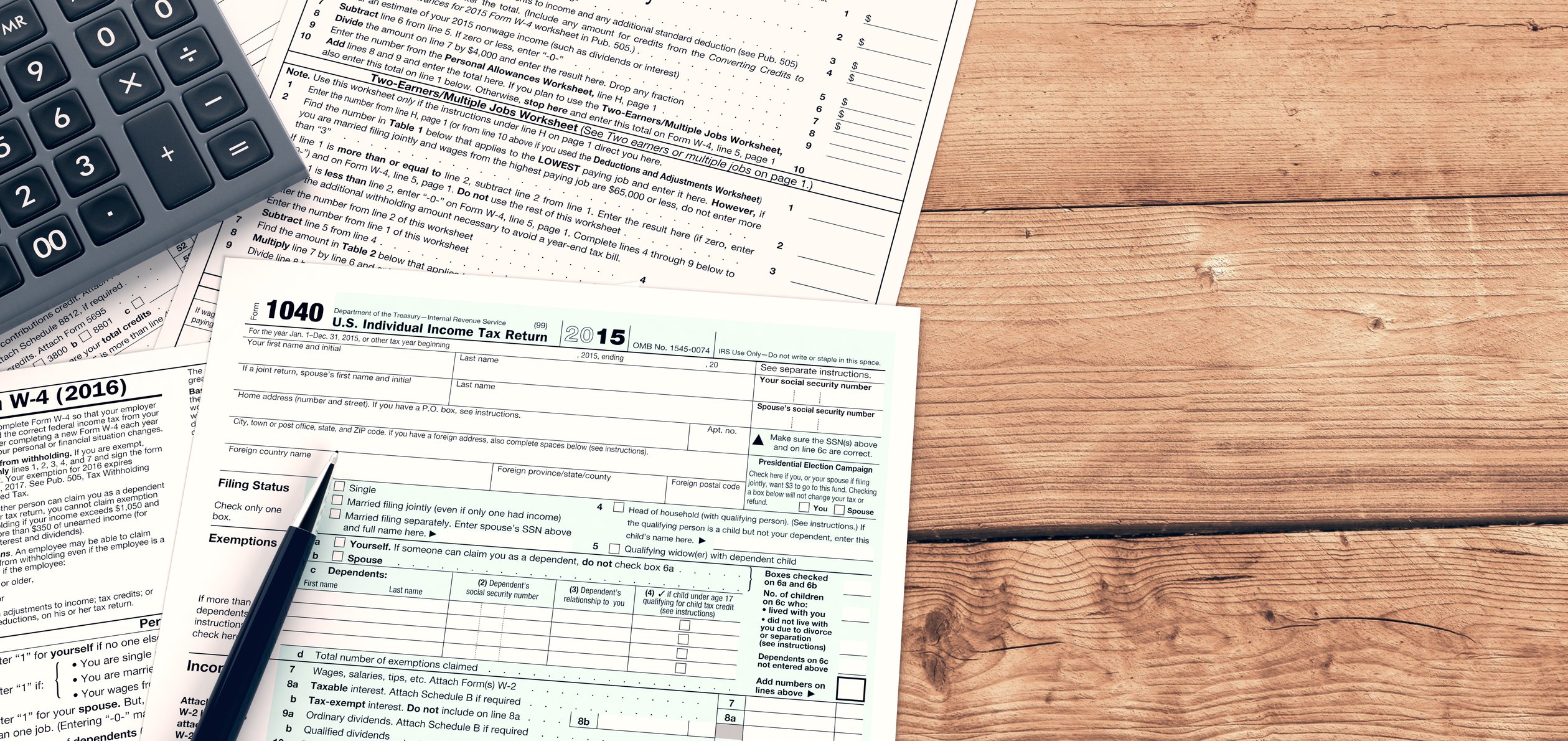 Tax forms, calculator, and pen on wooden surface