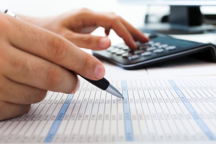 An accountant examining balance sheet figures with the aid of a calculator. 