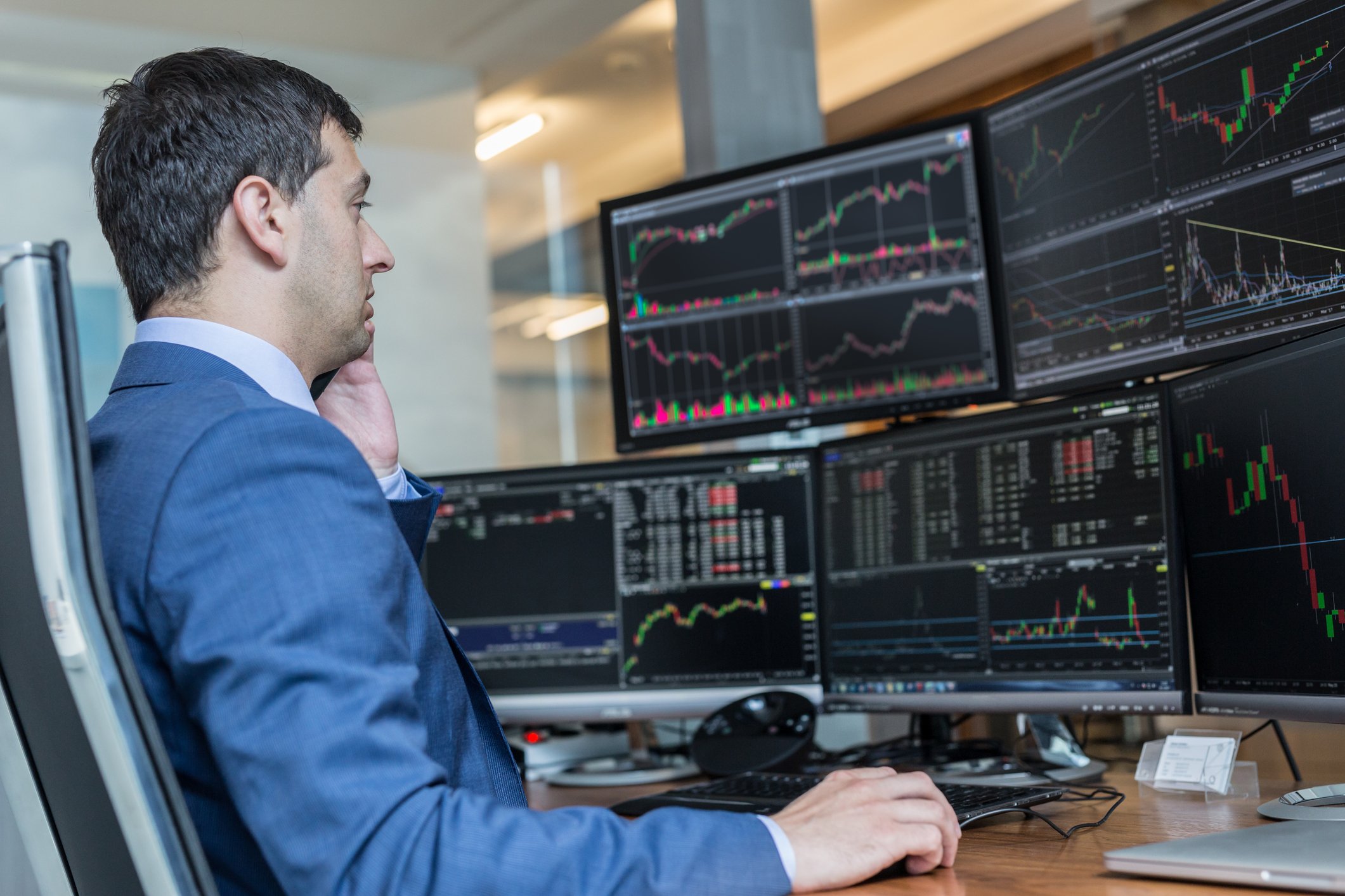 Stock trader sitting at a desk. with computer screens all around him. 