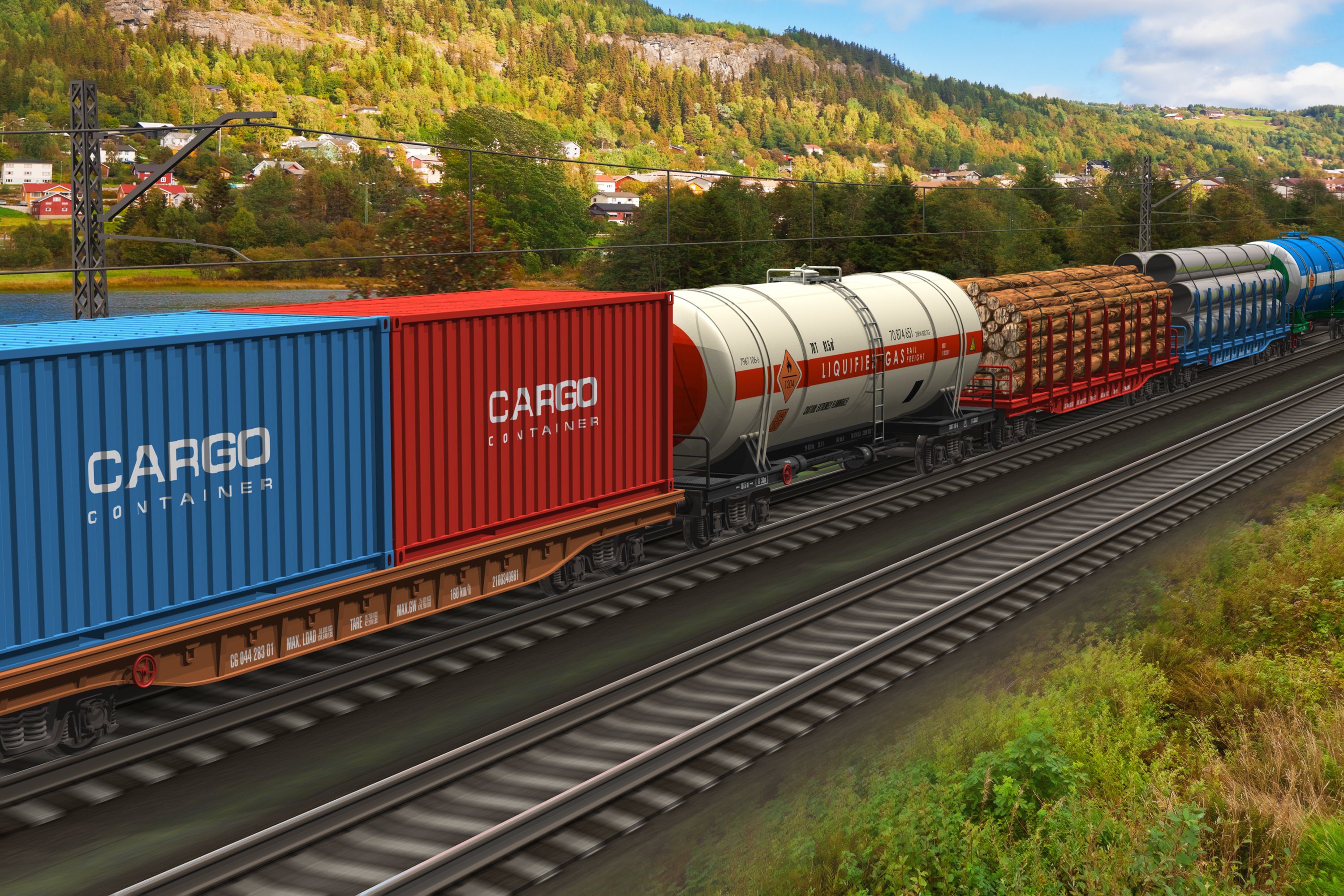 Freight train with assorted cargo rolling on tracks against a backdrop of greenery and houses.