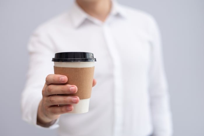 Man in collared shirt holding out to-go cup