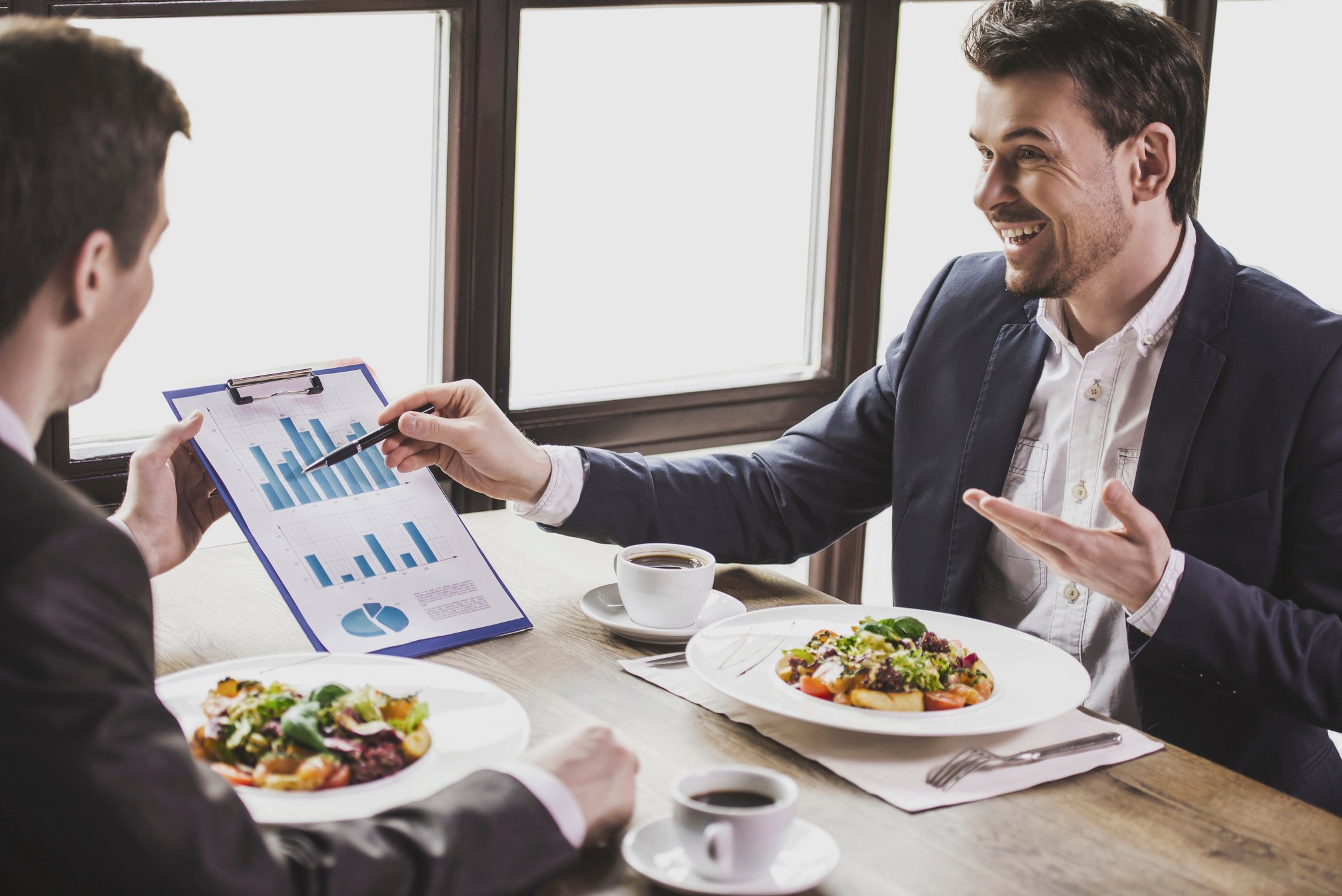 Men eating, conversing, and looking at charts.