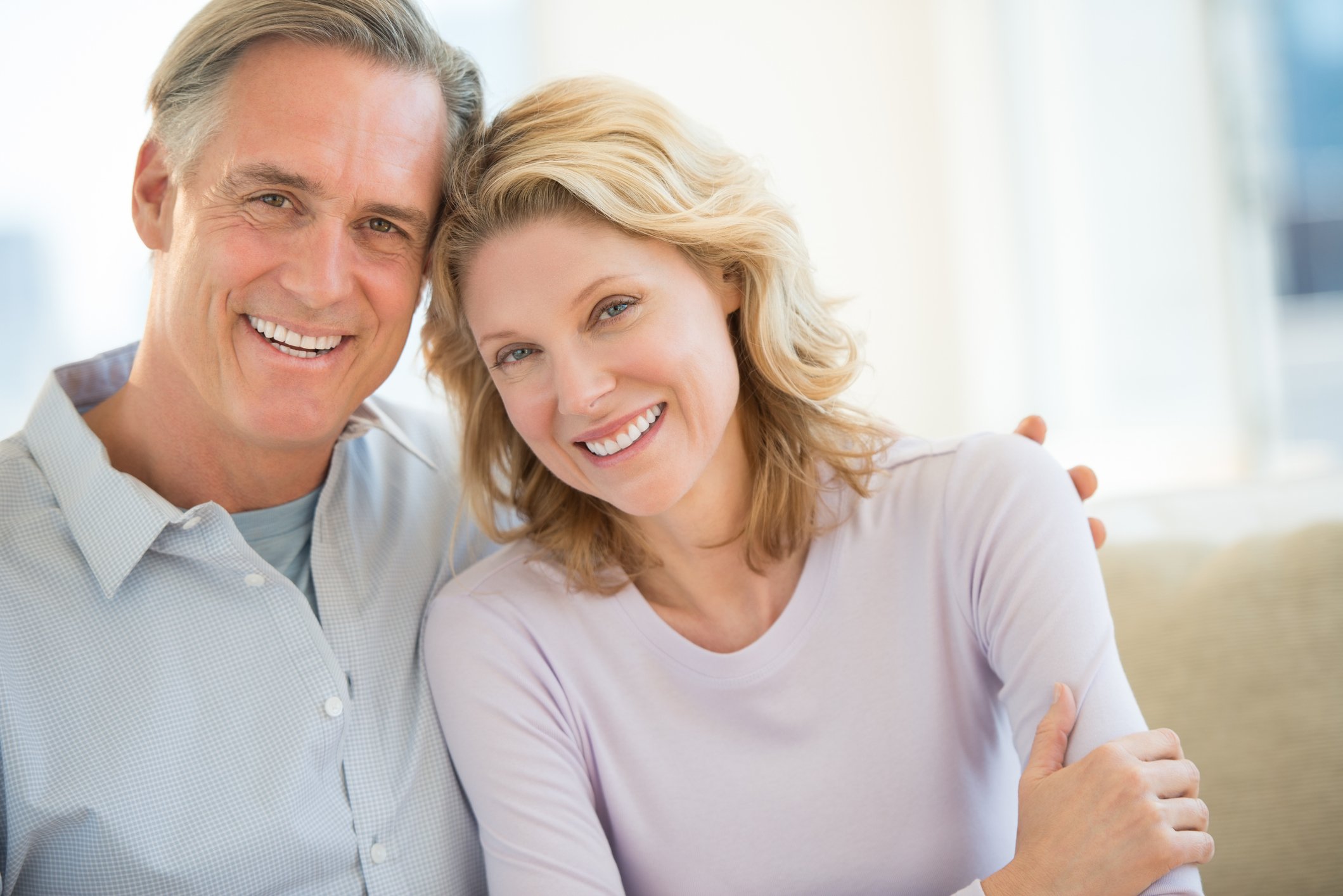 Smiling middle-aged couple sitting on a beige couch.