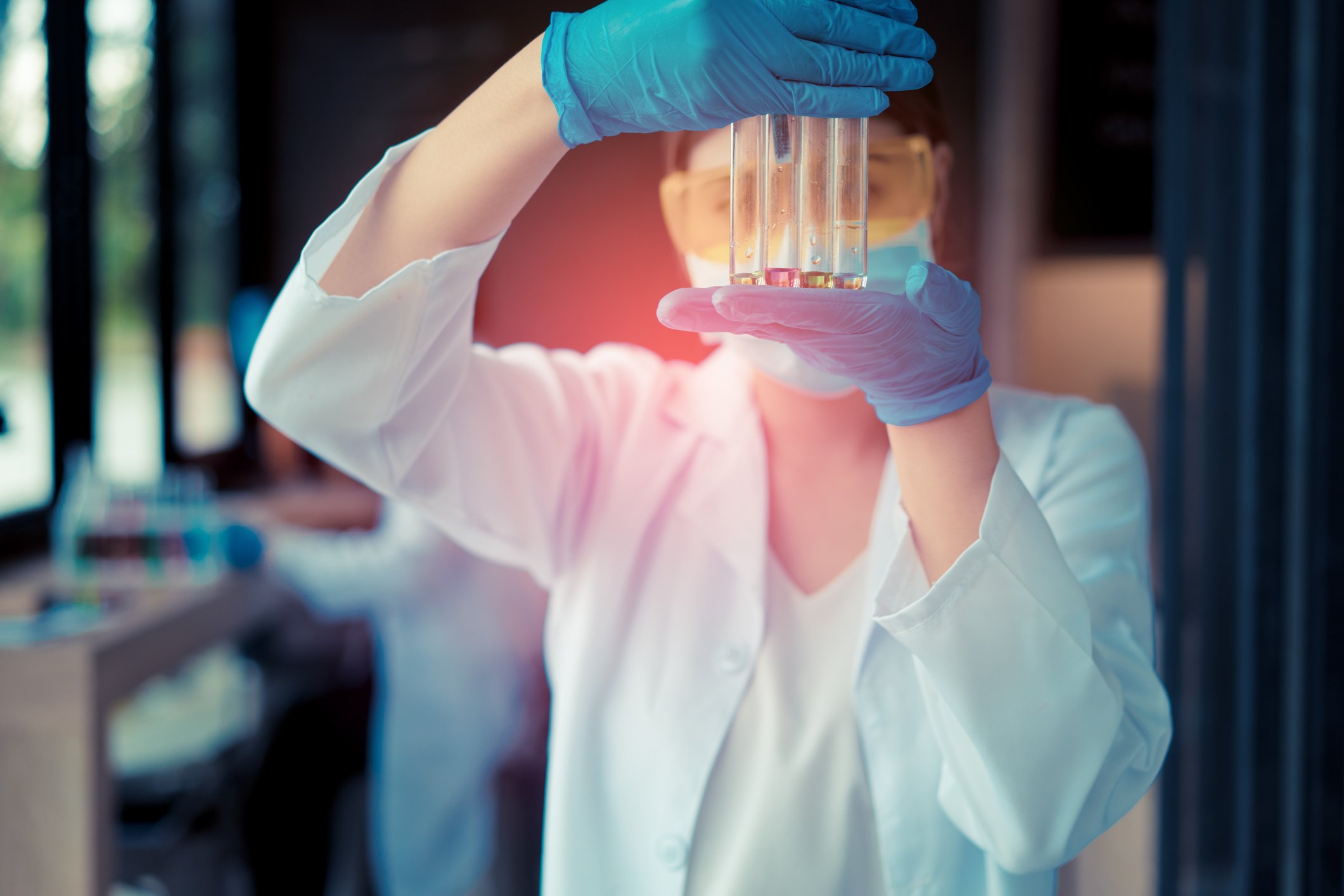 Laboratory worker holding test tubes in front of her protective eyewear.