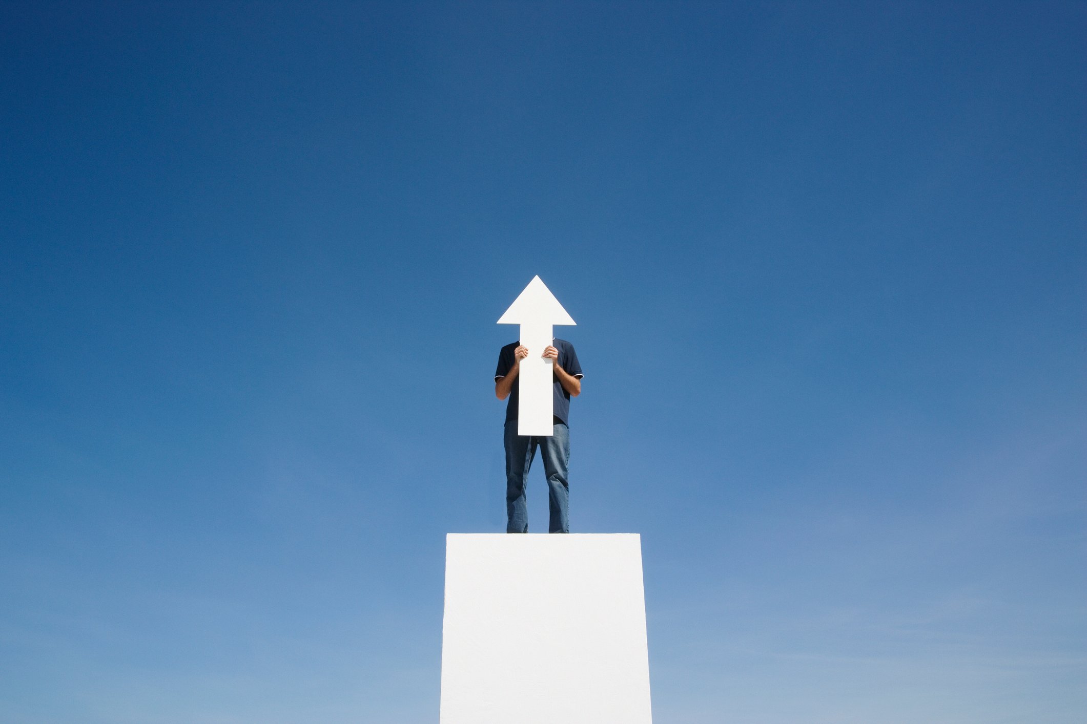 A man standing on a platform holding an arrow cut out pointing up