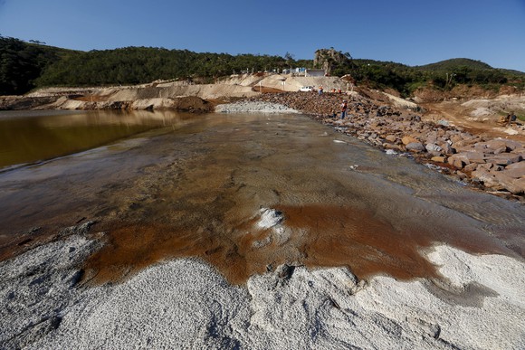 Tailings pond with brown water atop gray sand, with workers nearby.