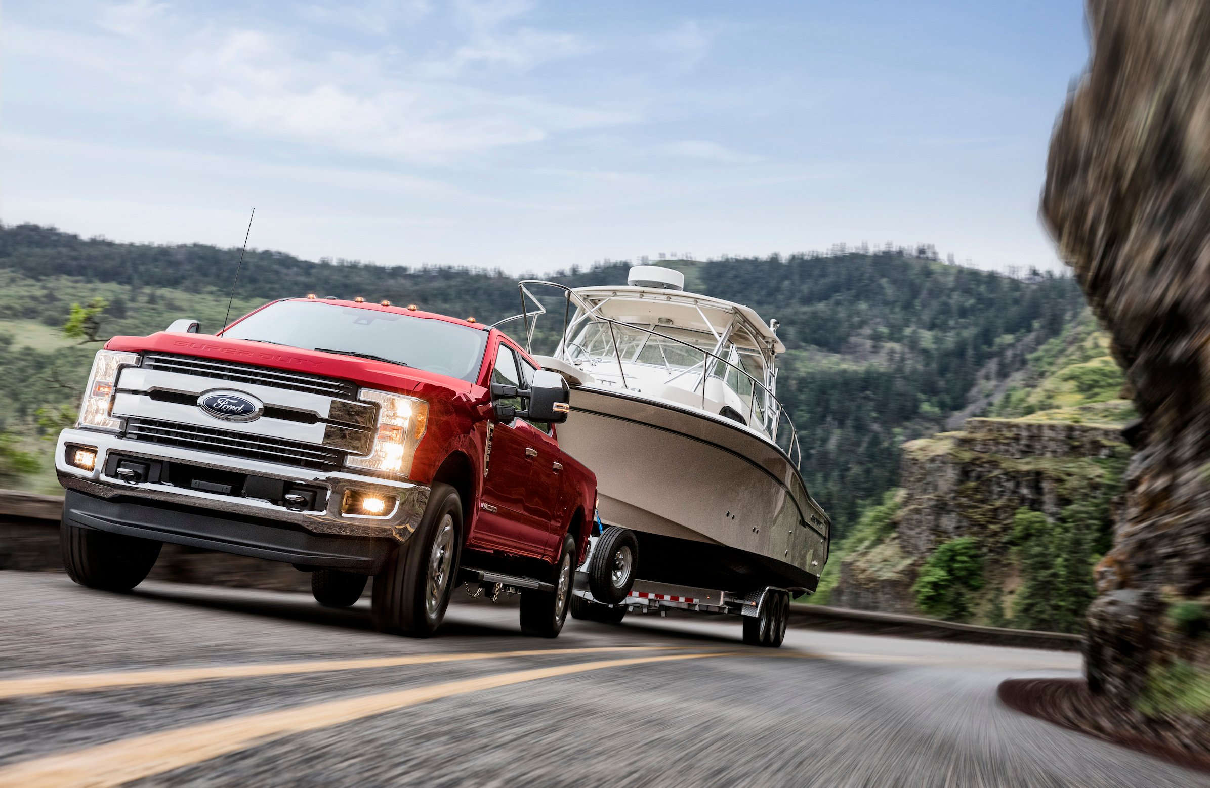 A red Ford F250 Lariat, a heavy-duty full-size pickup, towing a boat trailer up a mountain road. 