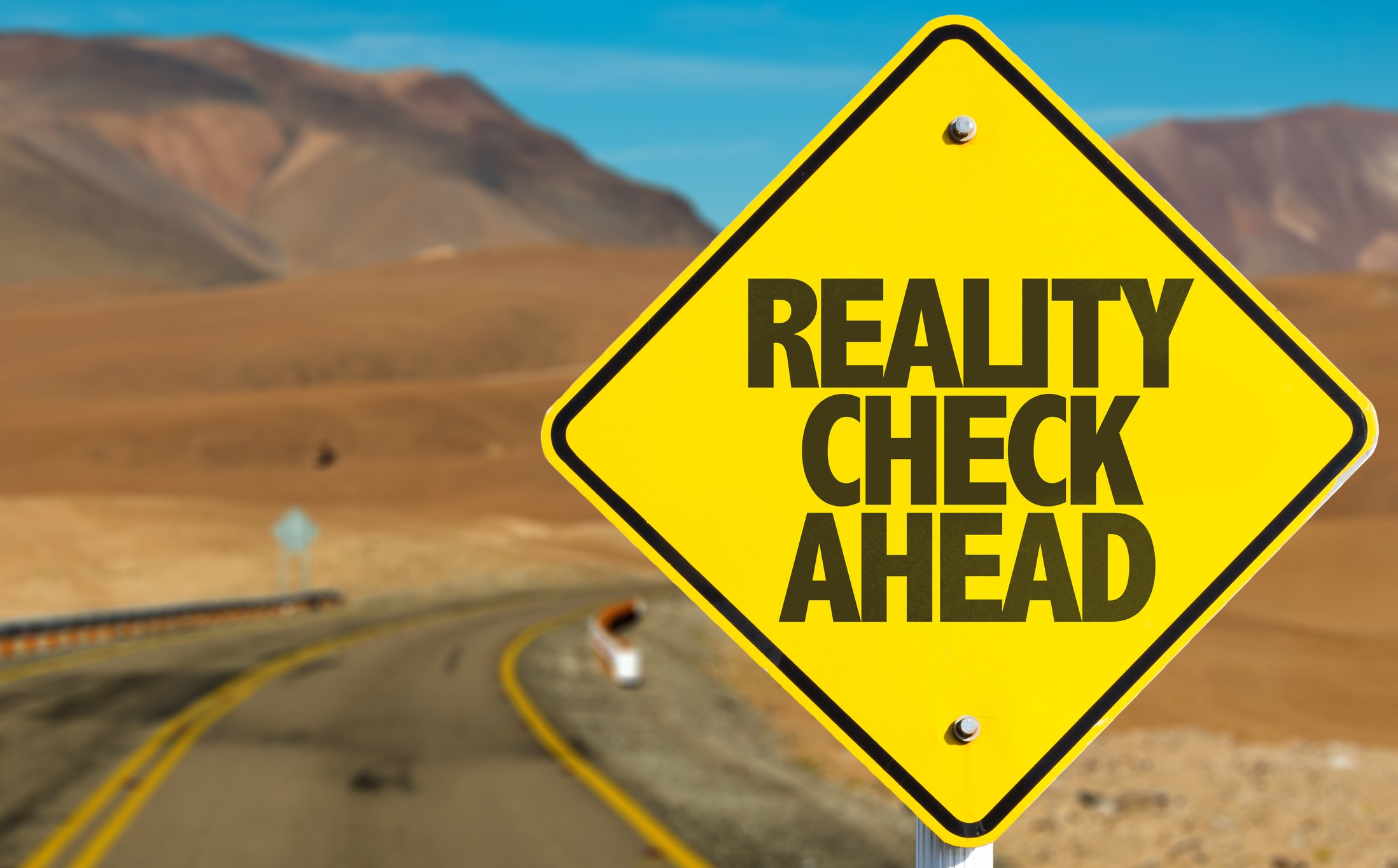 A "reality check ahead" sign on a deserted road.