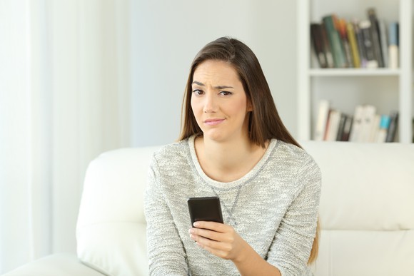A woman with a snarky expression sits on a chair, holding a cell phone