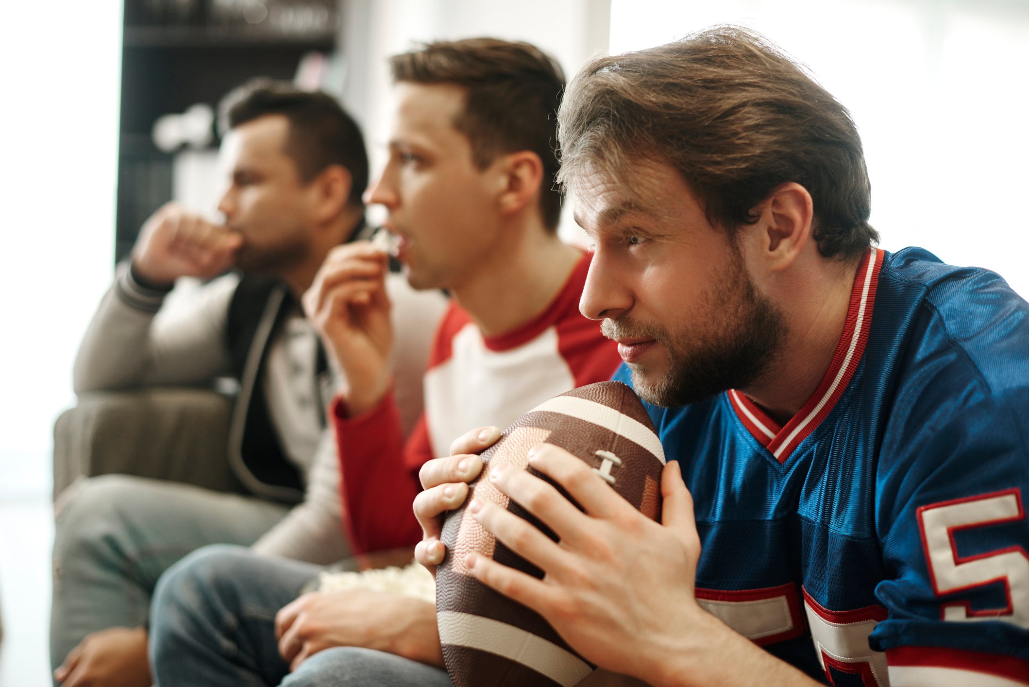 Three men sit on a couch with one holding a football.