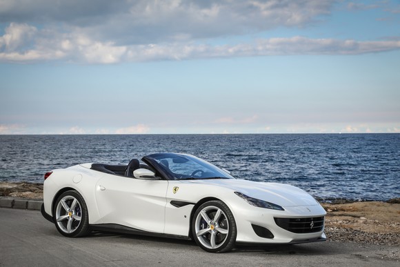 A white Ferrari Portofino, a two-seat front-engined convertible sports car, parked by the ocean. 