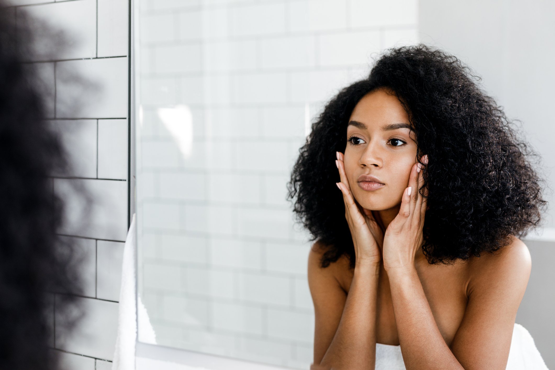 A woman looking in the bathroom mirror and touching her face.