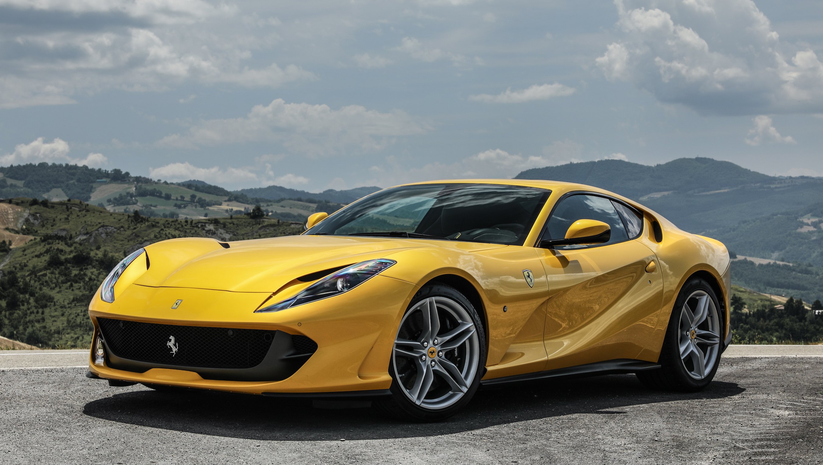 A yellow Ferrari 812 Superfast, a two-seat front-engined sports car, parked on a mountain road. 