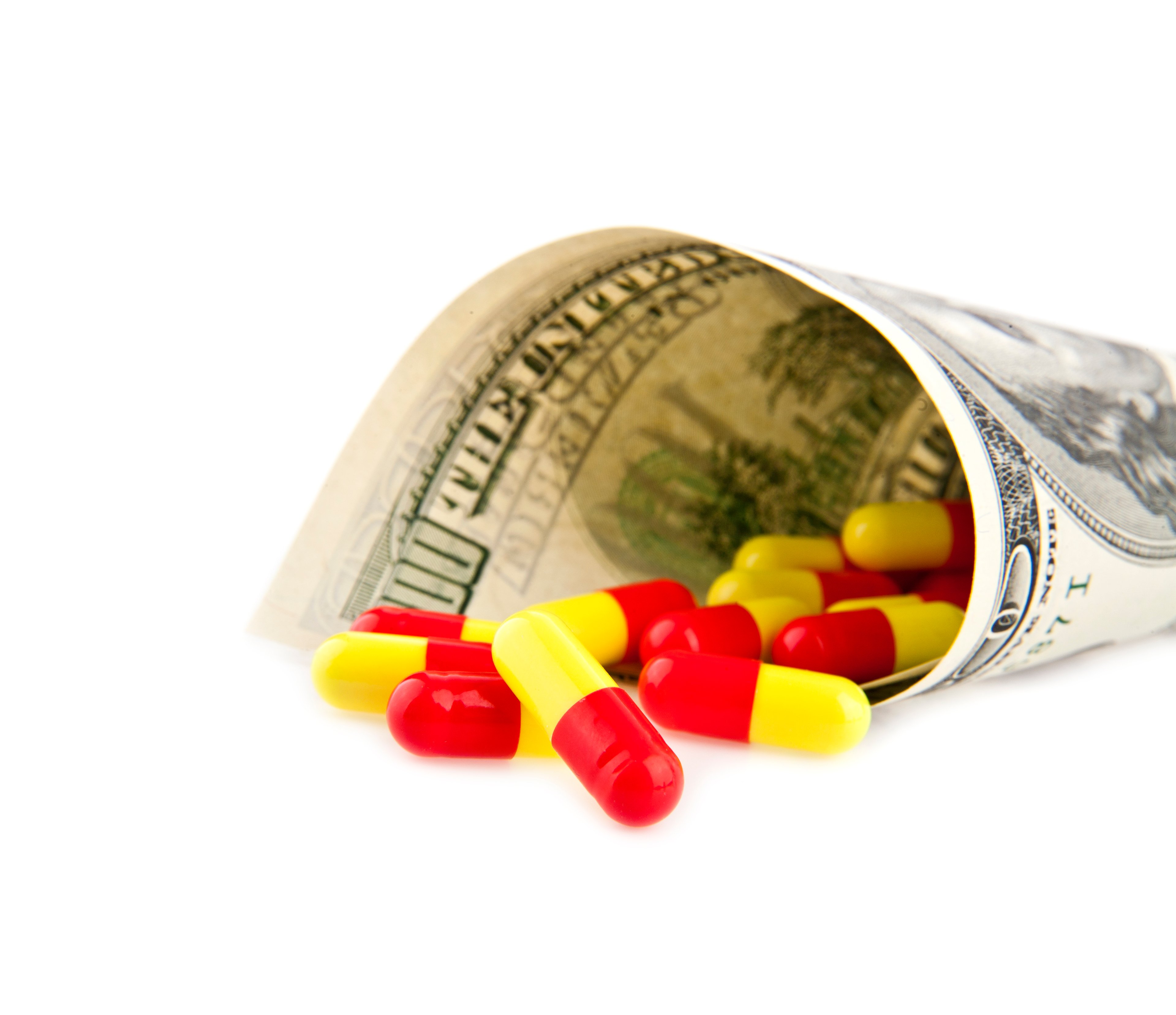 Bright capsules tumbling from a rolled-up hundred dollar bill.