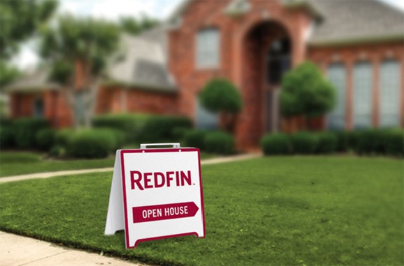 An "open house" sign with a Redfin logo on the lawn of a home for sale.