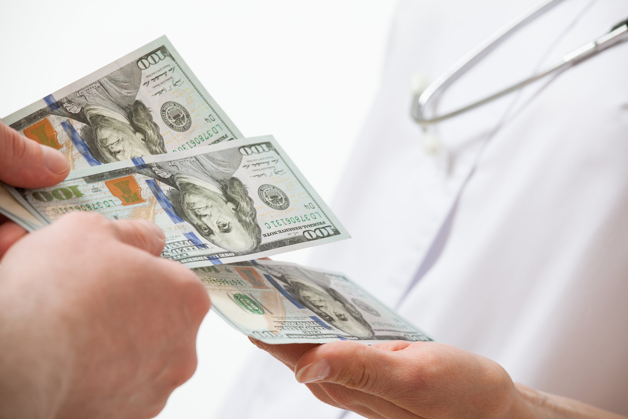 Pair of hands passing several $100 bills to a doctor.