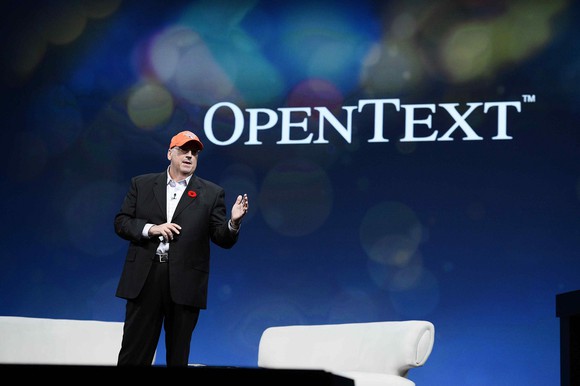 Person wearing hat on a stage with OpenText logo behind him.