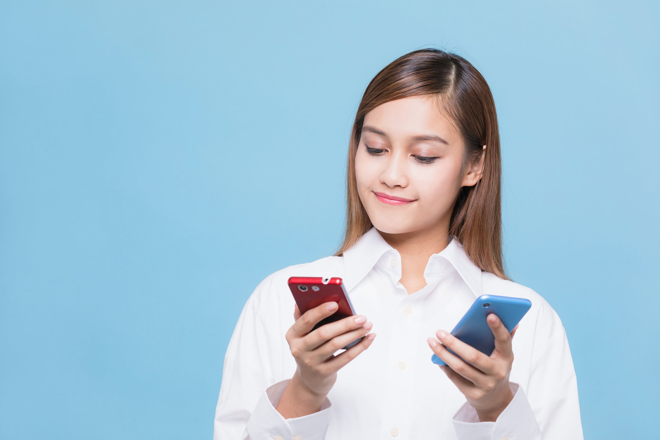 A young woman smiling comparing two smartphones.