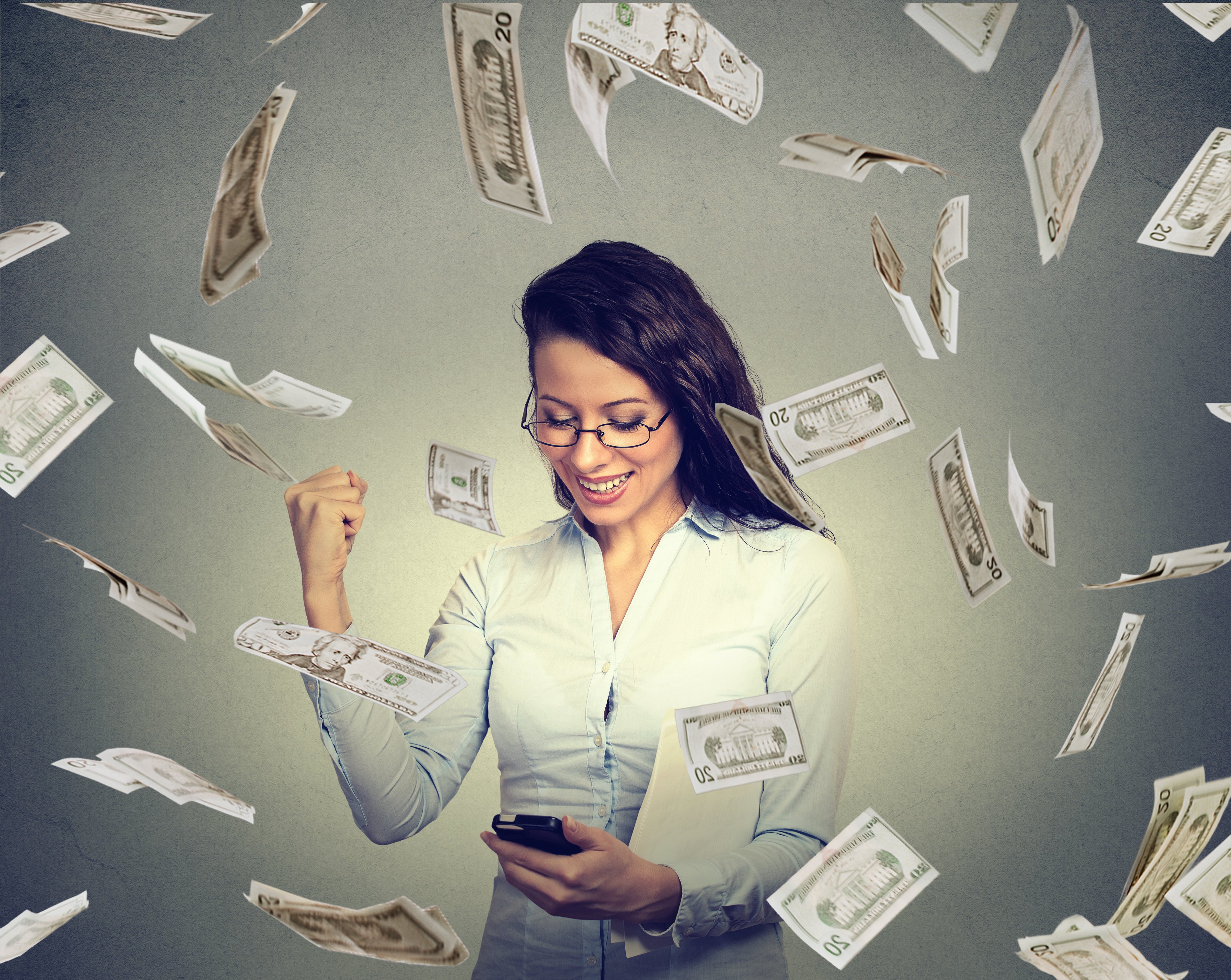 A woman looking happily at a phone while $20 bills rain down around her